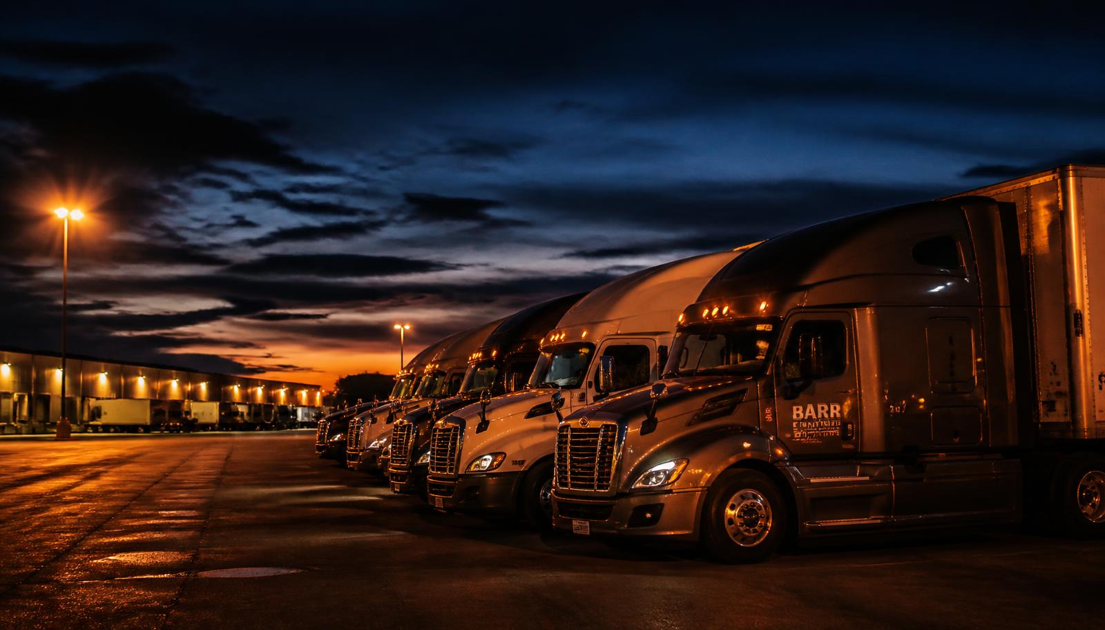 Row of semi trucks parked in a lit trucking yard at dusk